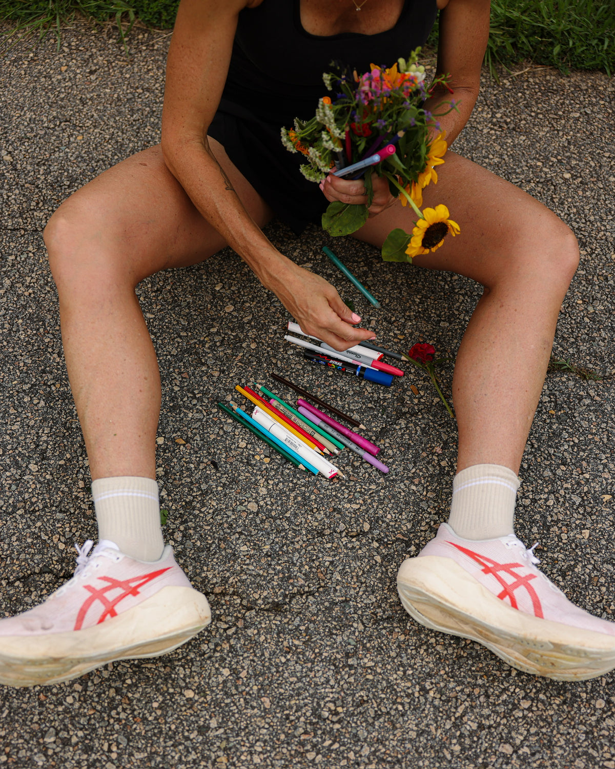 Runner sitting on pavement with a bunch of wildflowers and coloured pens scattered around her running shoes