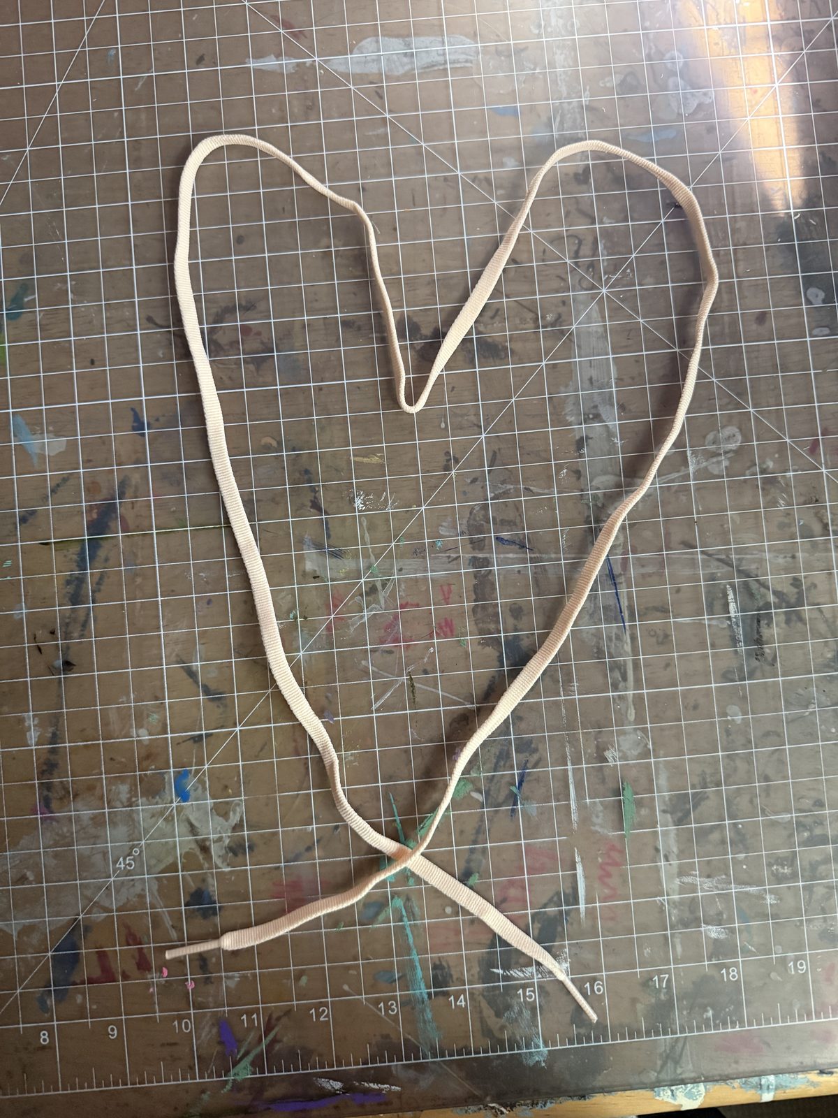 A shoelace laid out in the shape of a heart on a paint-splattered studio table